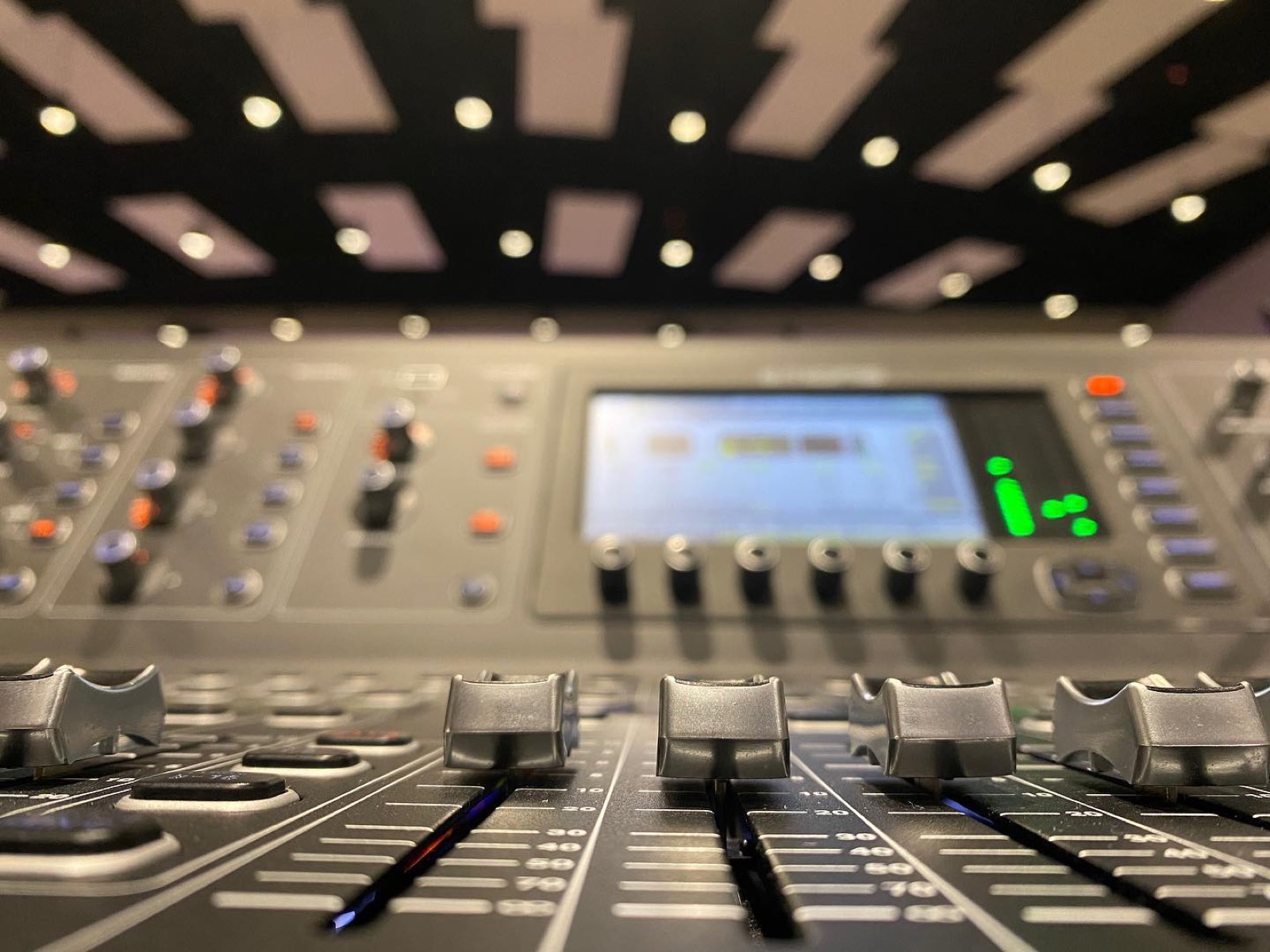 Digital mixing console faders in focus with warm house lights overhead during a church service